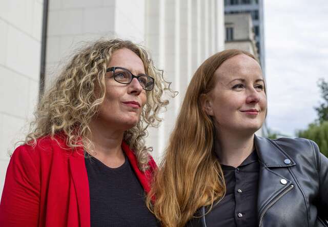 Two women look into the distance, the city in the background.